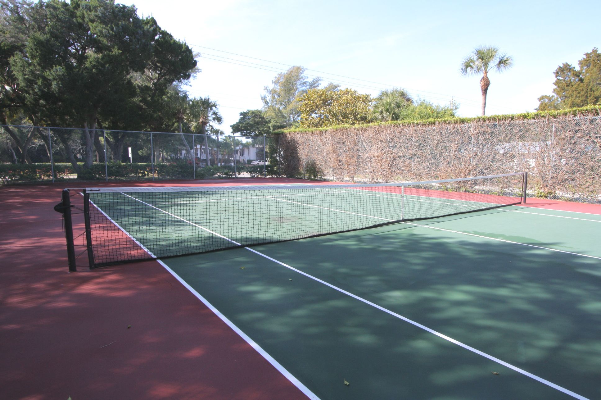 Un court de tennis avec un filet, entouré d’arbres et d’un mur de pierre.