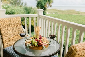 A round glass table with a charcuterie board, two glasses of red wine, wicker chairs, and a white railing with a view of the ocean. - Beach Castle Resort by RVA (Longboat Key)