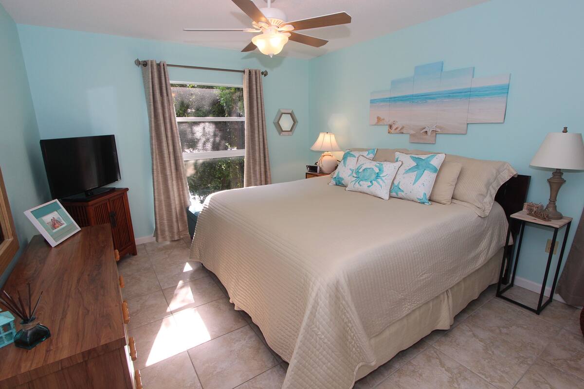A bedroom with a bed, a television, a desk, and a window with curtains.