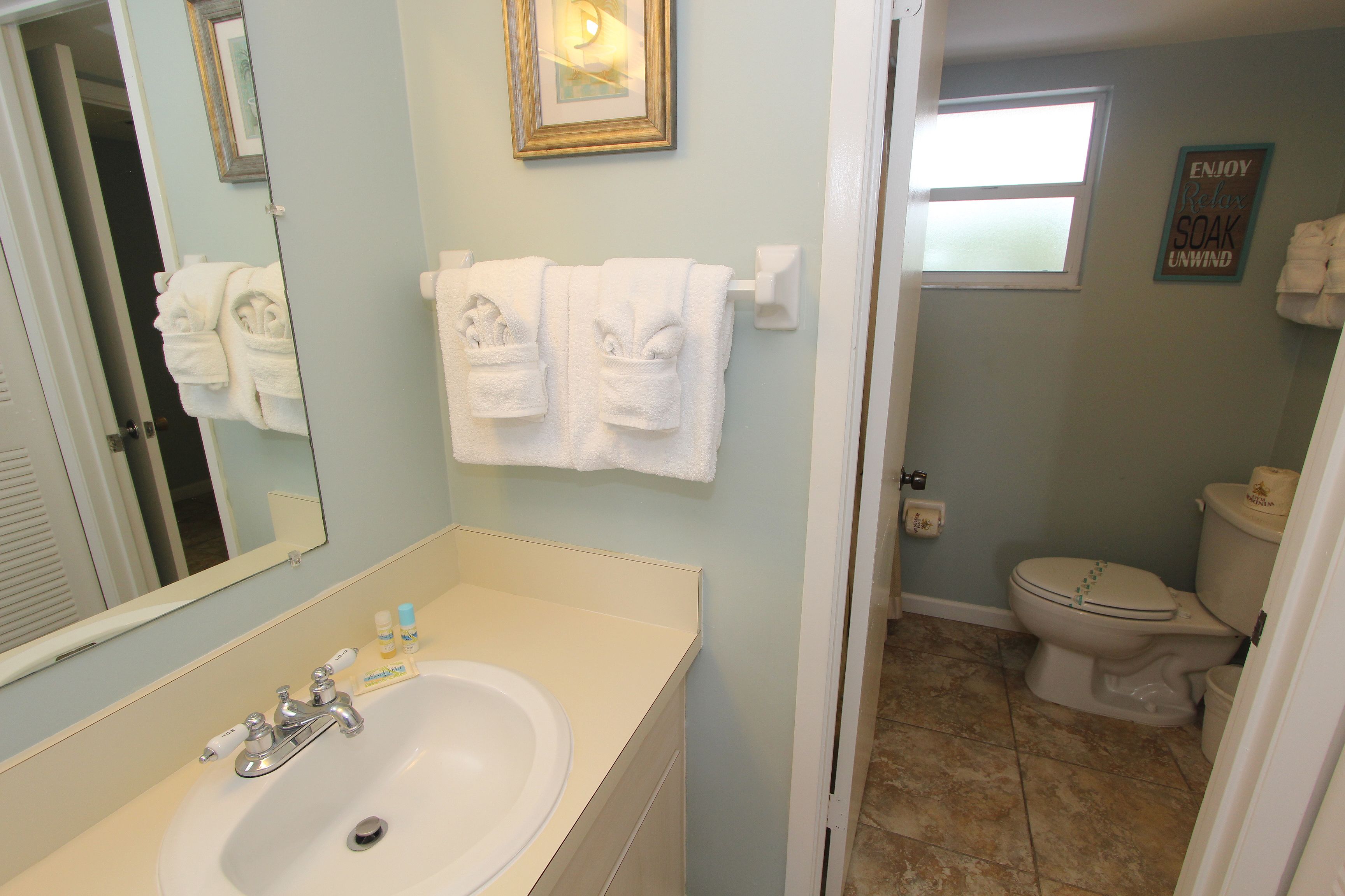 A bathroom with a sink, mirror, towels, and a toilet.