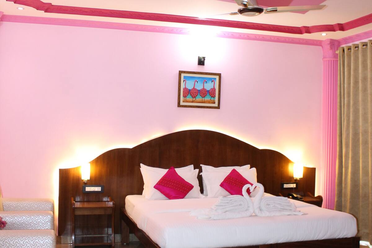 Habitación de hotel con una cama grande, dos mesitas de noche, un ventilador de techo y un cuadro en la pared.