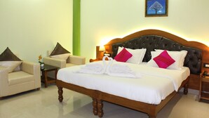 Una habitación de hotel elegante con una cama grande, dos sillones, una mesita y una mesita de noche.