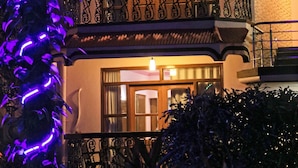 Un edificio de dos pisos con balcones, luz cálida en el interior y una lámpara decorativa morada a la izquierda.