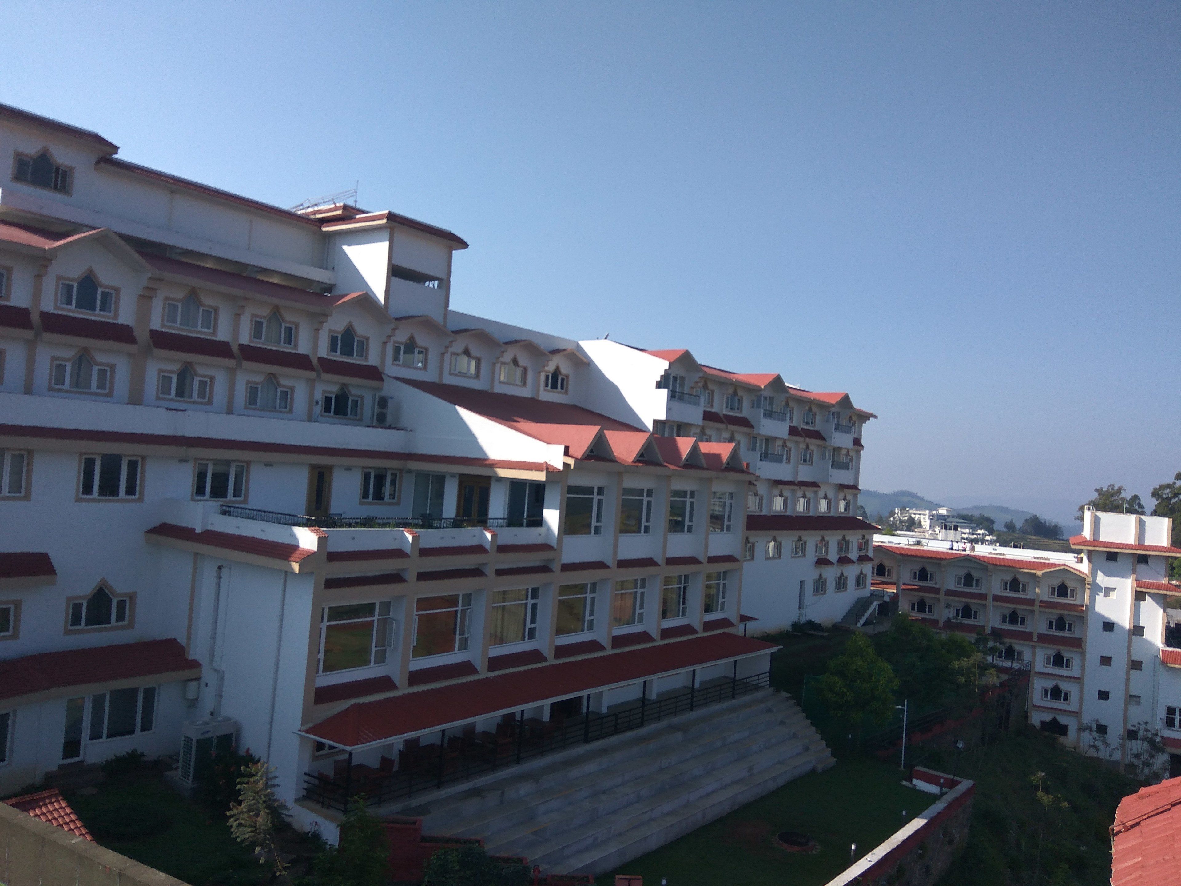 A multi-story hotel with a red roof and white walls, featuring balconies and large windows.
