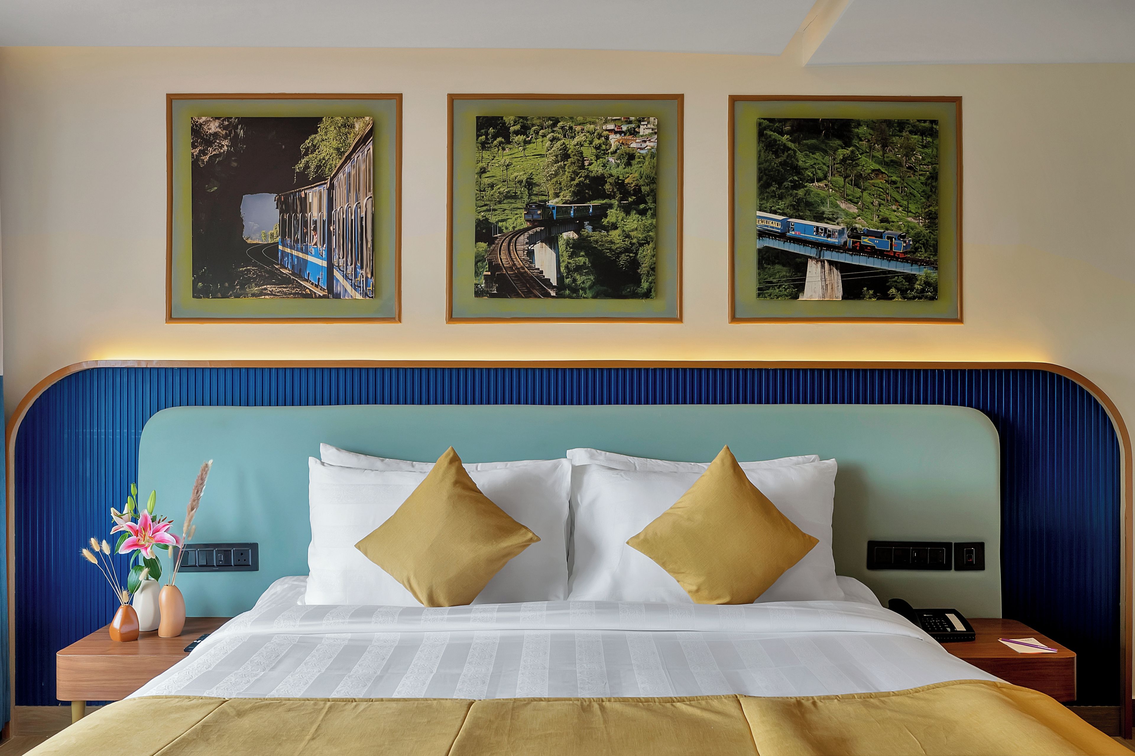 A hotel room with a bed, two pillows, a nightstand, a lamp, and three framed pictures on the wall.