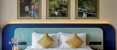 A hotel room with a bed, two pillows, a nightstand, a lamp, and three framed pictures on the wall.