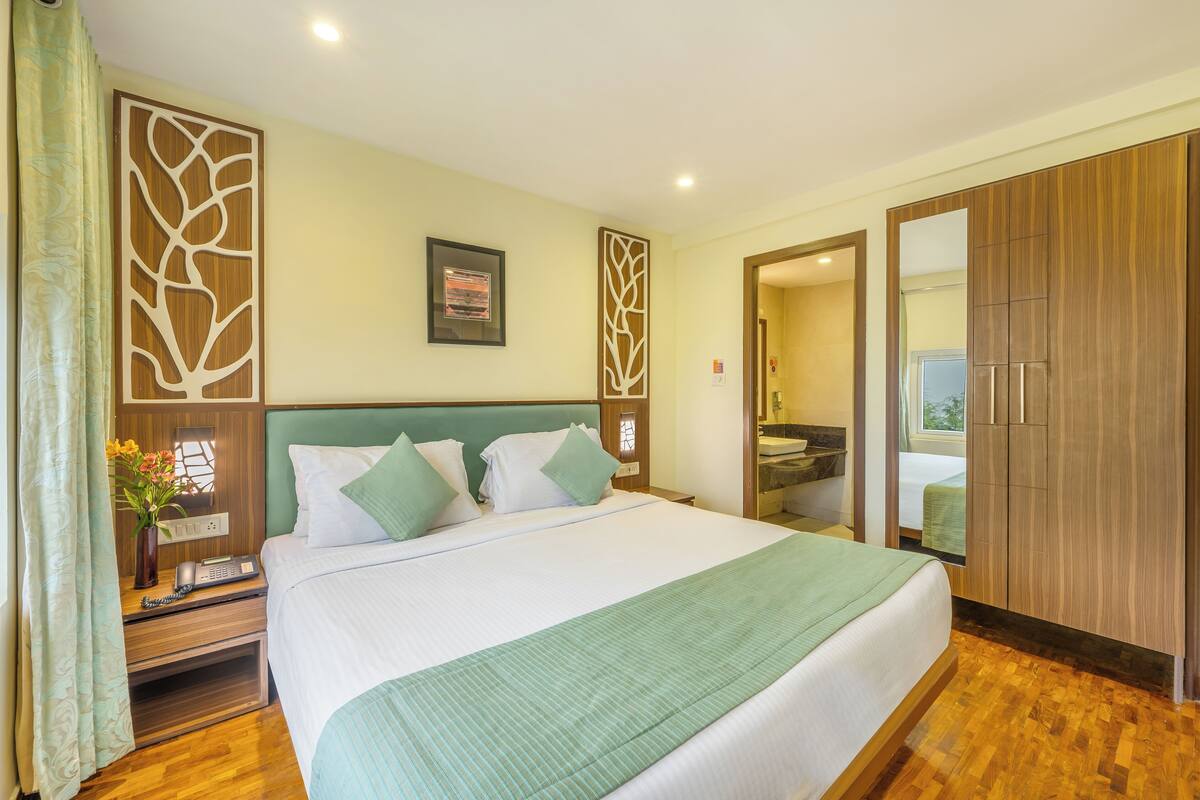 Une chambre d’hôtel avec un grand lit, une tête de lit en bois, une couvre-lit verte et une armoire en bois.