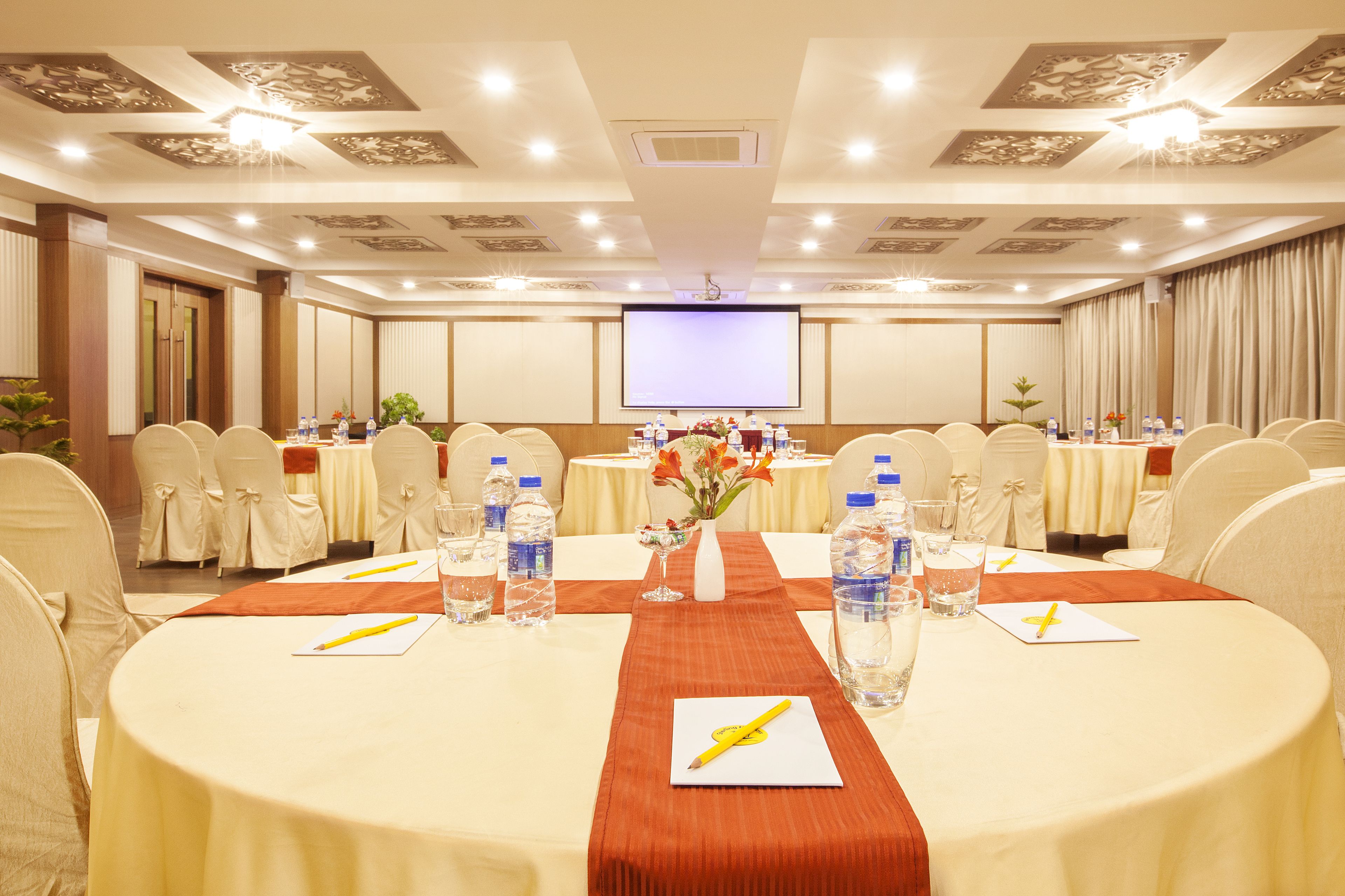 A conference room with round tables, chairs, water bottles, and a projector screen.