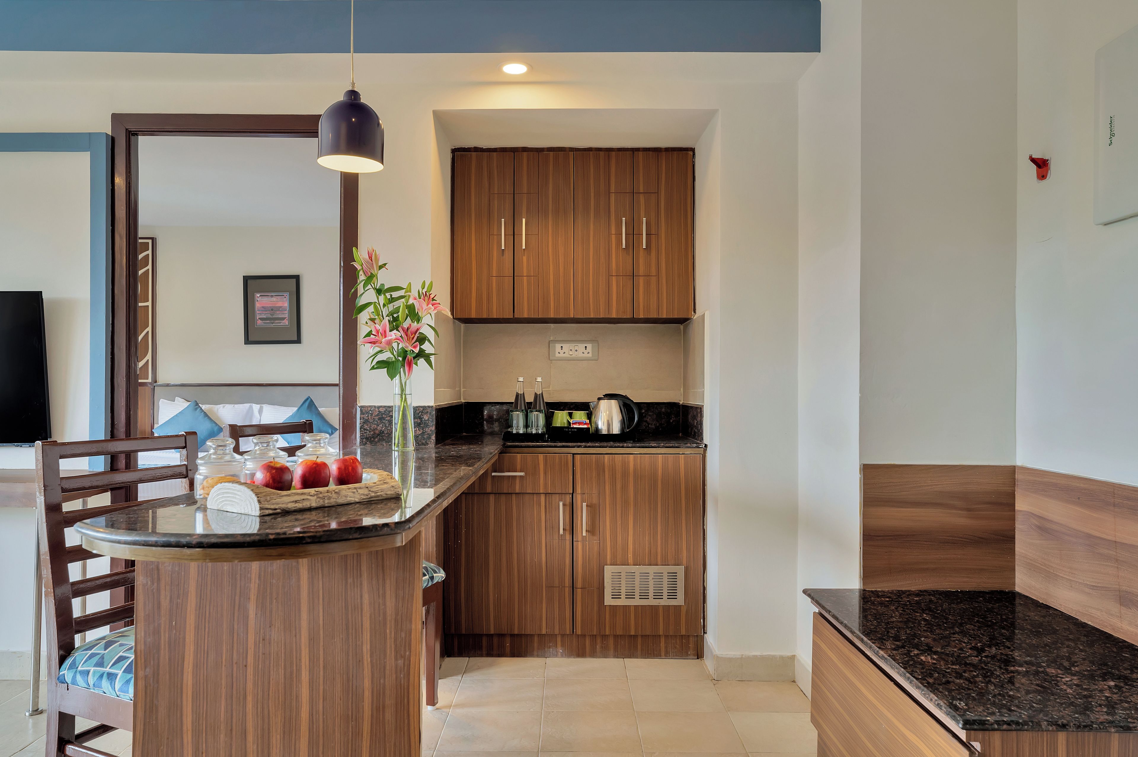 A modern kitchen with wooden cabinets, a marble countertop, and a dining area with a chair and table.