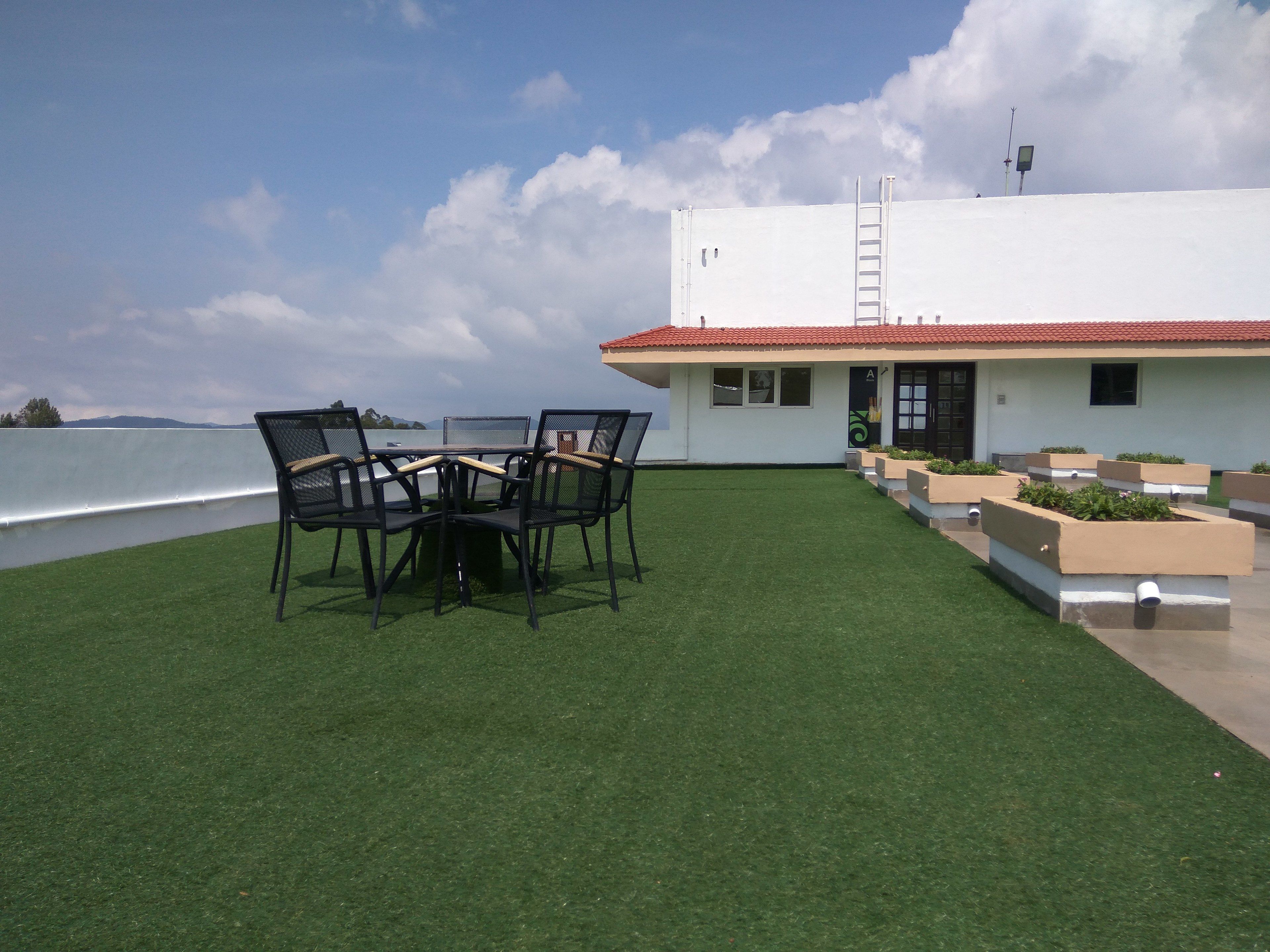 A patio with a table and chairs, a white building with a red roof, and a view of the water.