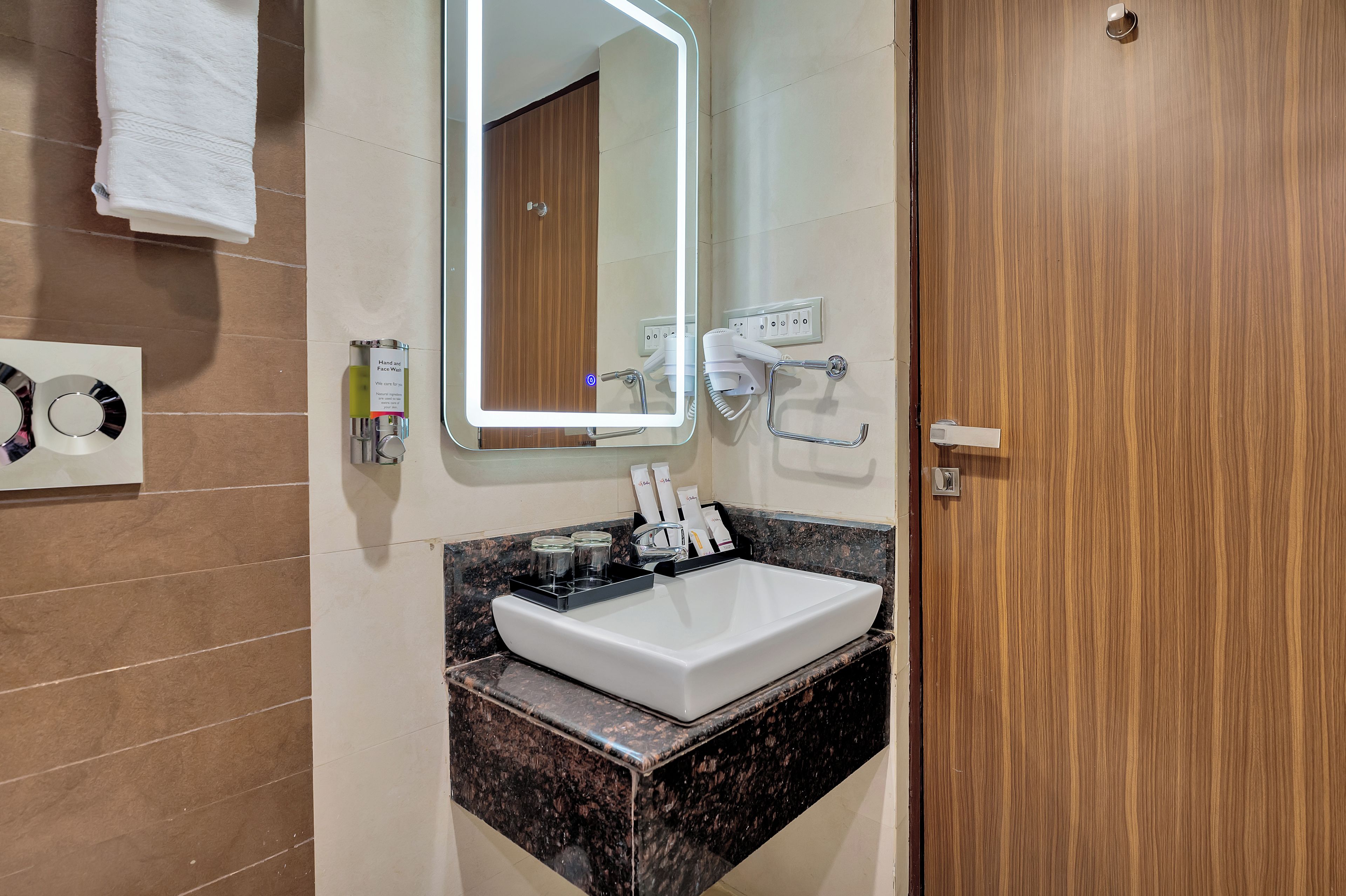 Une salle de bain avec un lavabo blanc, un miroir, un sèche-cheveux et un porte-serviettes.