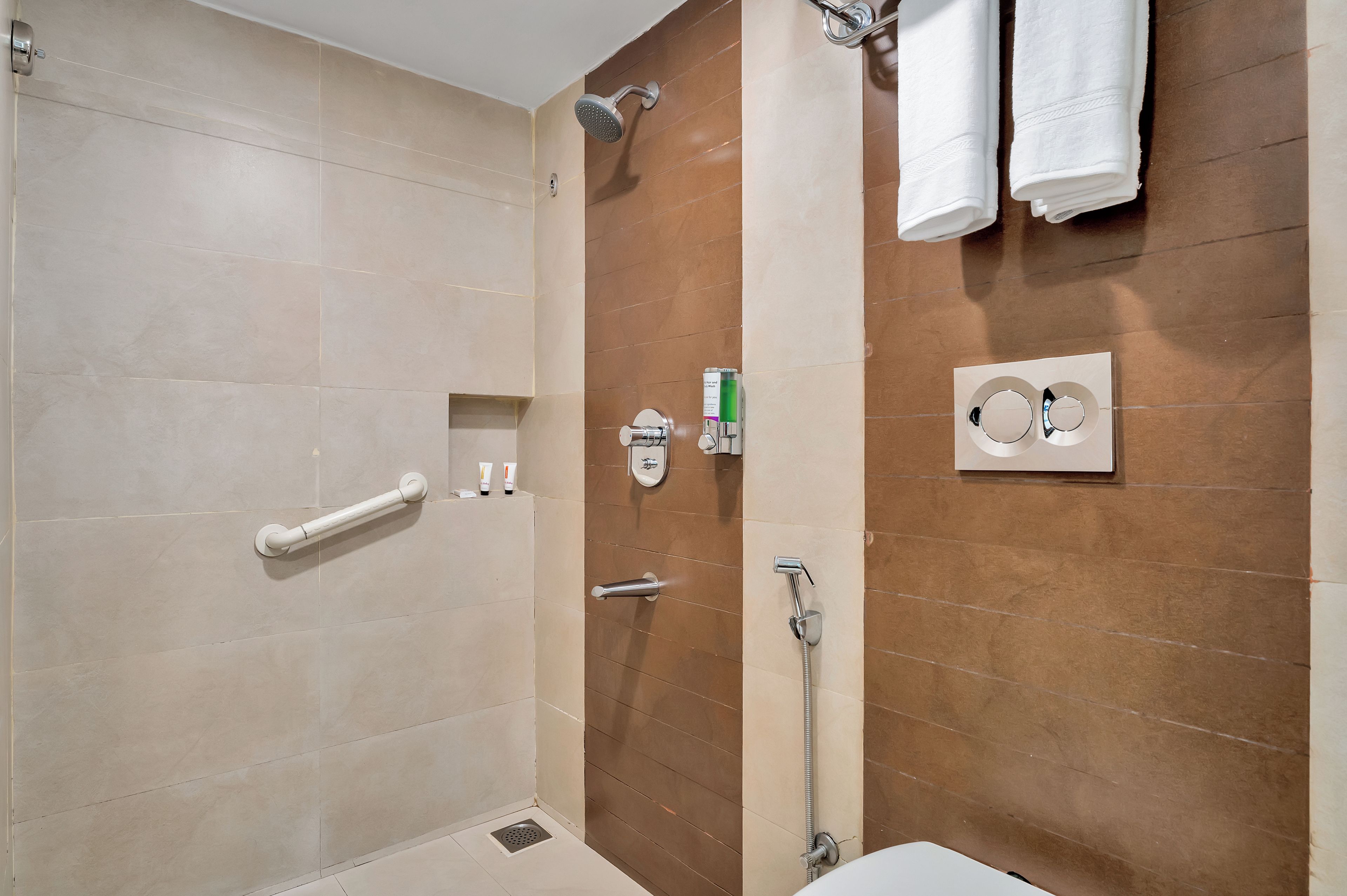 A bathroom with a shower, a toilet, a towel rack, and a soap dispenser.
