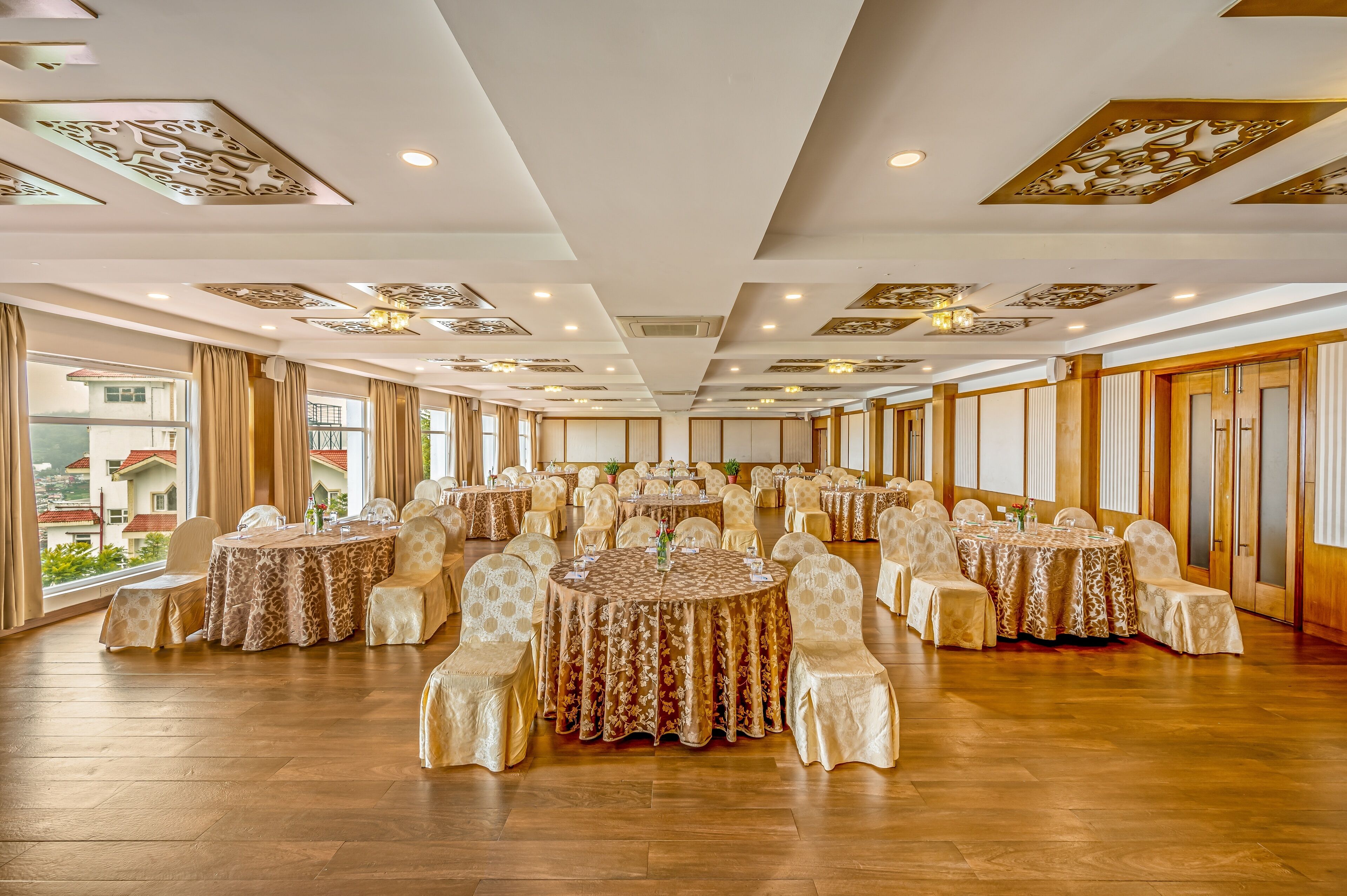 Une salle de banquet avec de nombreuses tables rondes, chacune recouverte d’une nappe à motifs, entourée de chaises rembourrées.