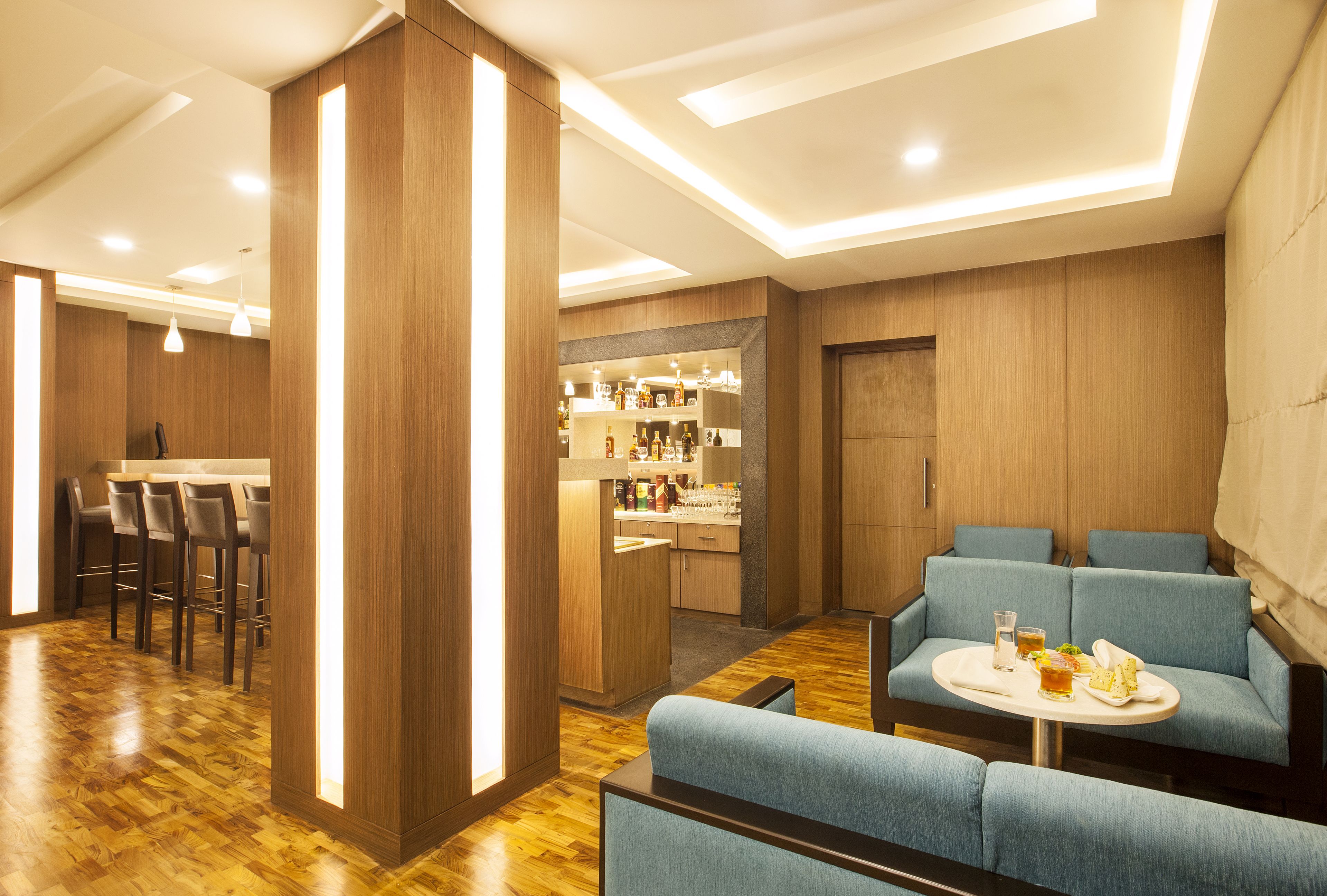 Un espace bar moderne avec un plancher en bois, des tabourets de bar et un coin salon doté de canapés bleus recouverts de tissu.
