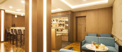 Un espace bar moderne avec un plancher en bois, des tabourets de bar et un coin salon doté de canapés bleus recouverts de tissu.