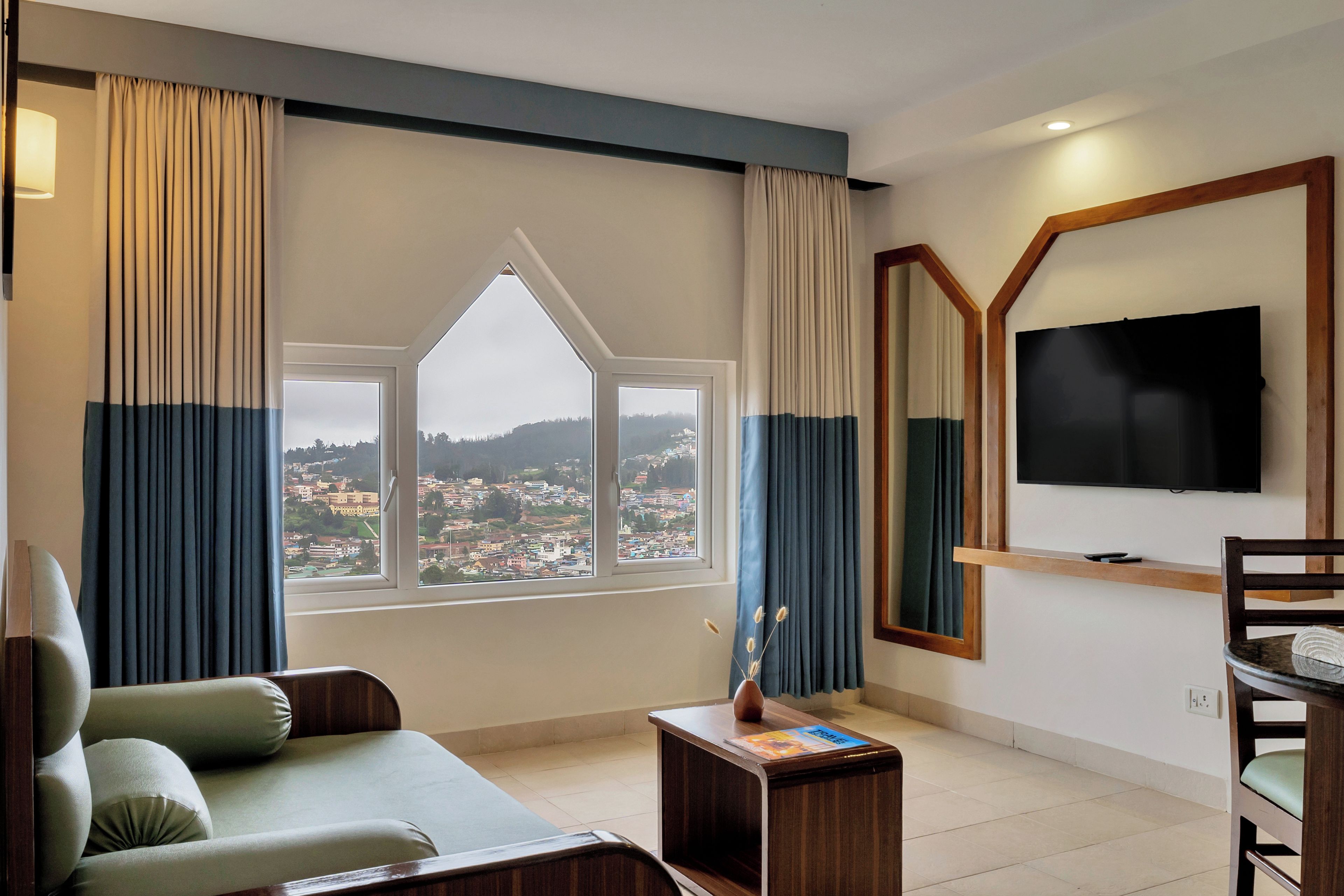 Habitación de hotel con un ventanal grande, un televisor de pantalla plana, un sofá, una mesita y una silla.