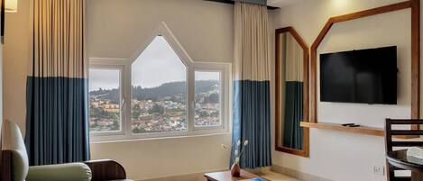 Habitación de hotel con un ventanal grande, un televisor de pantalla plana, un sofá, una mesita y una silla.