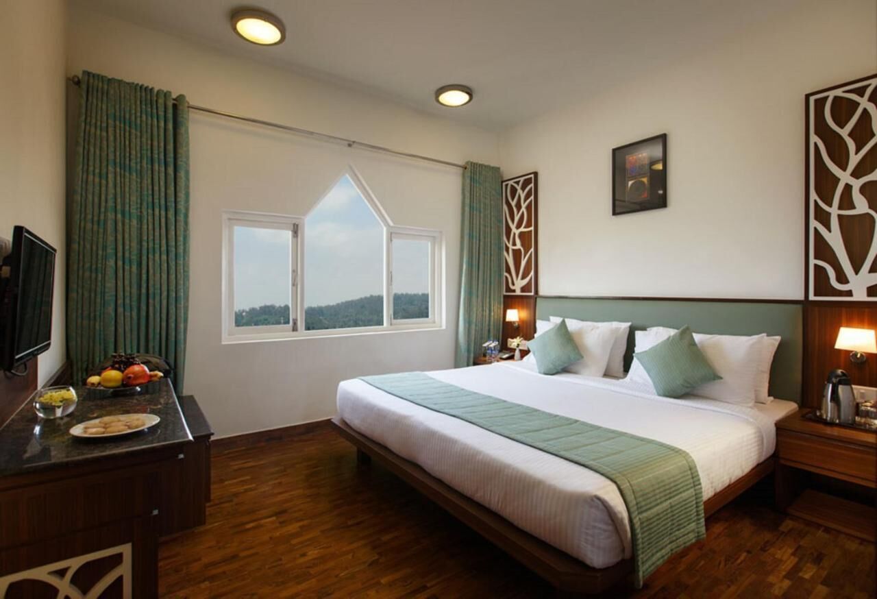 Habitación de hotel con una cama grande, un escritorio con frutero, una ventana con vistas y un adorno de pared.