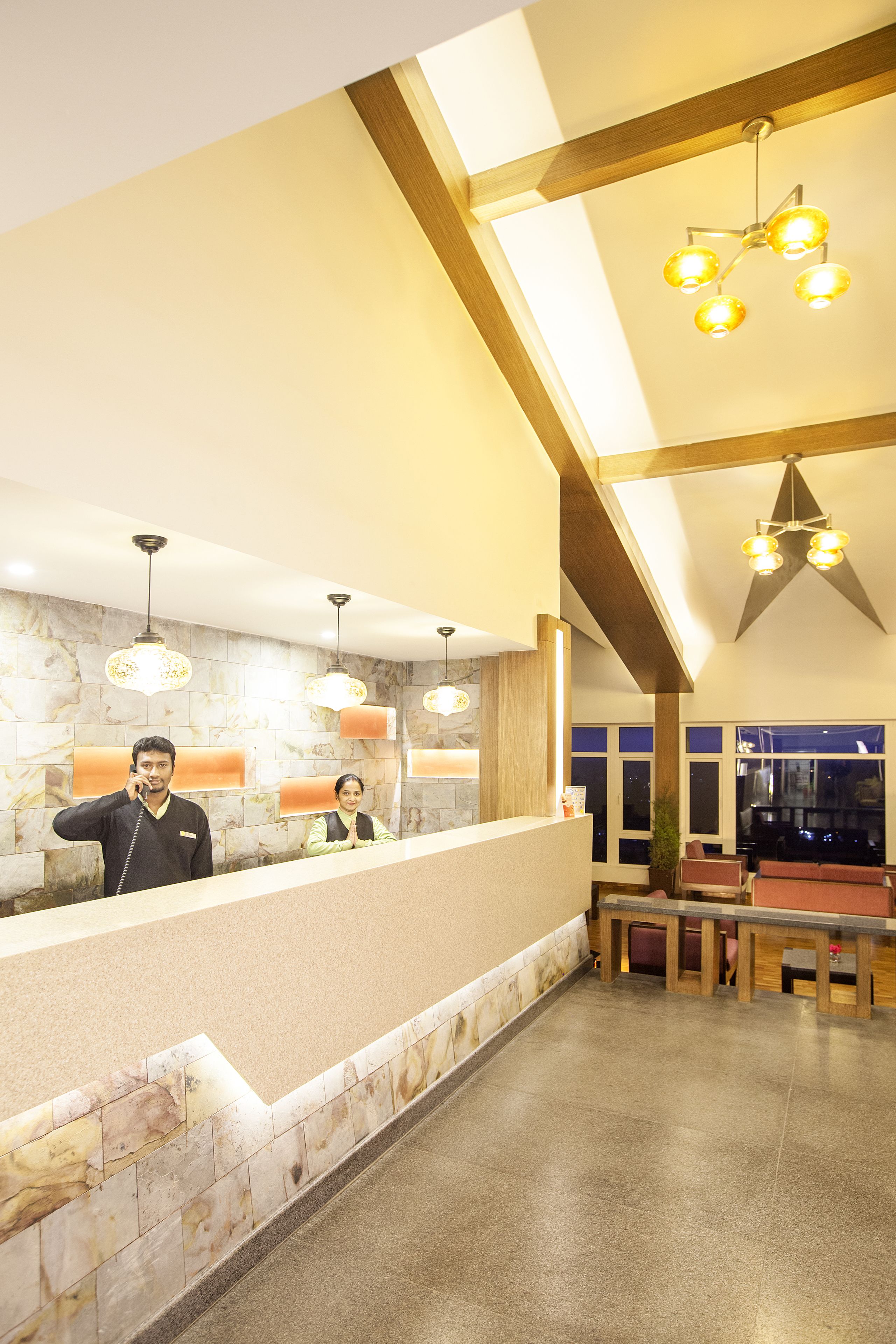 A hotel reception area with a marble wall, a reception desk, and a seating area with tables and chairs.