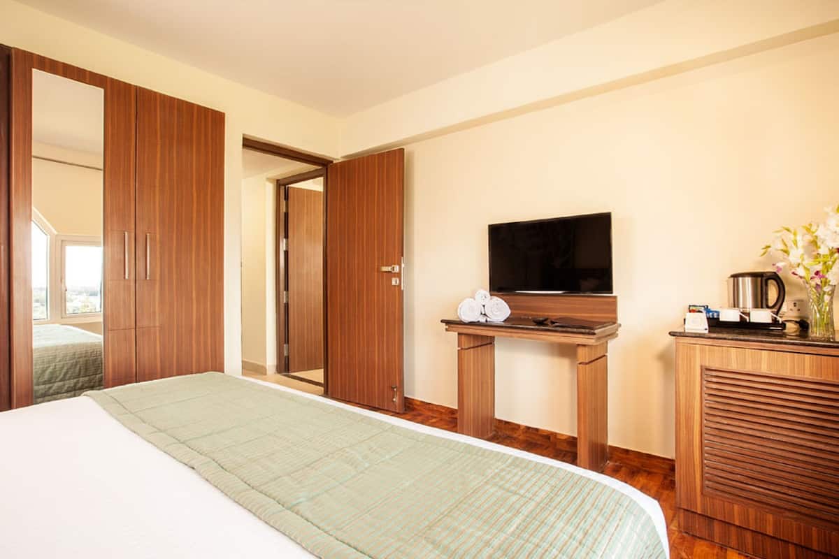 Une chambre d’hôtel comprenant un lit, une armoire en bois, un bureau avec un téléviseur à écran plat et un coin cuisine.