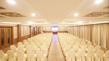 A conference room with rows of white chairs, a stage at the front, and a projector screen.