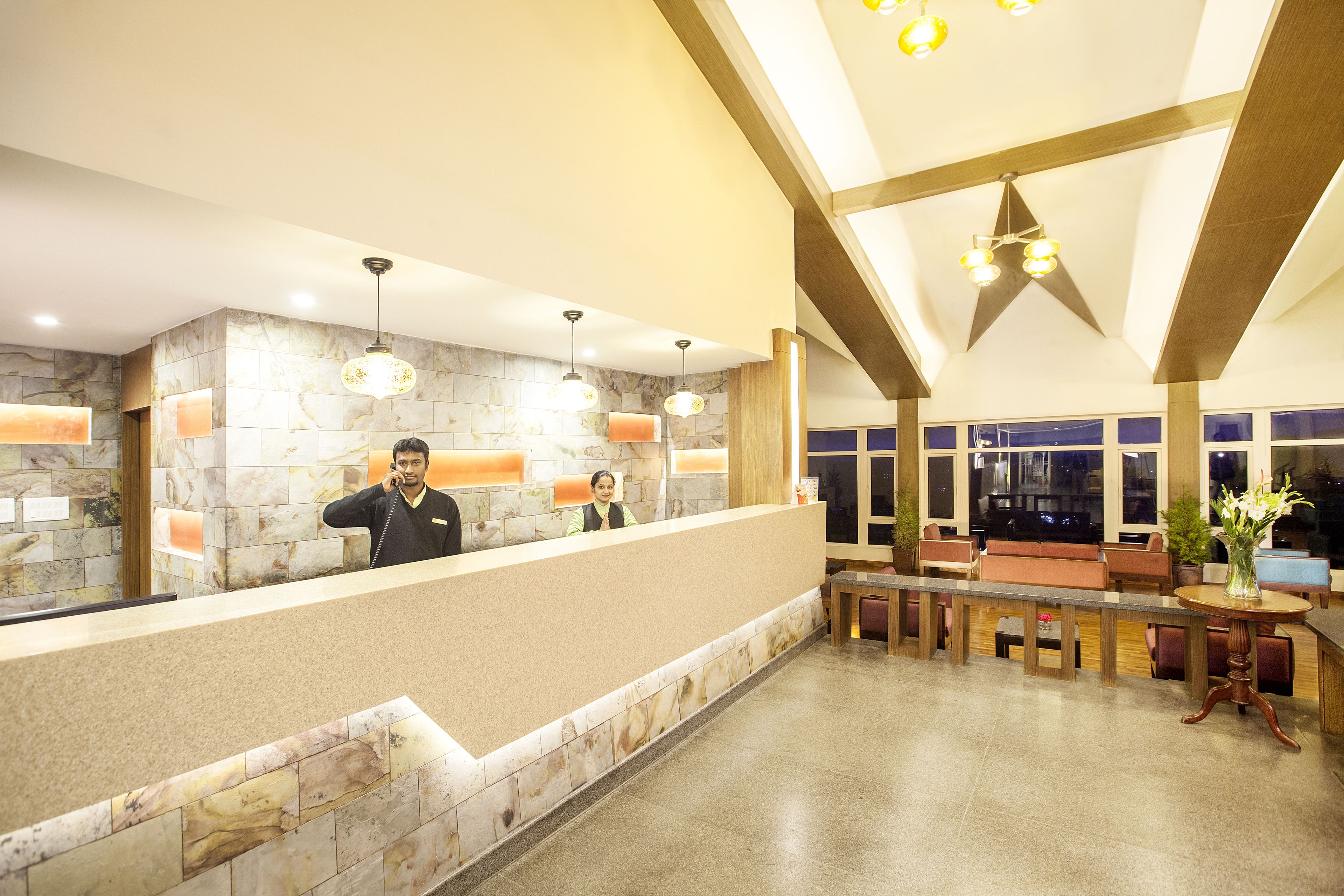 A hotel reception area with a marble wall, a reception desk, seating area, and a large window.