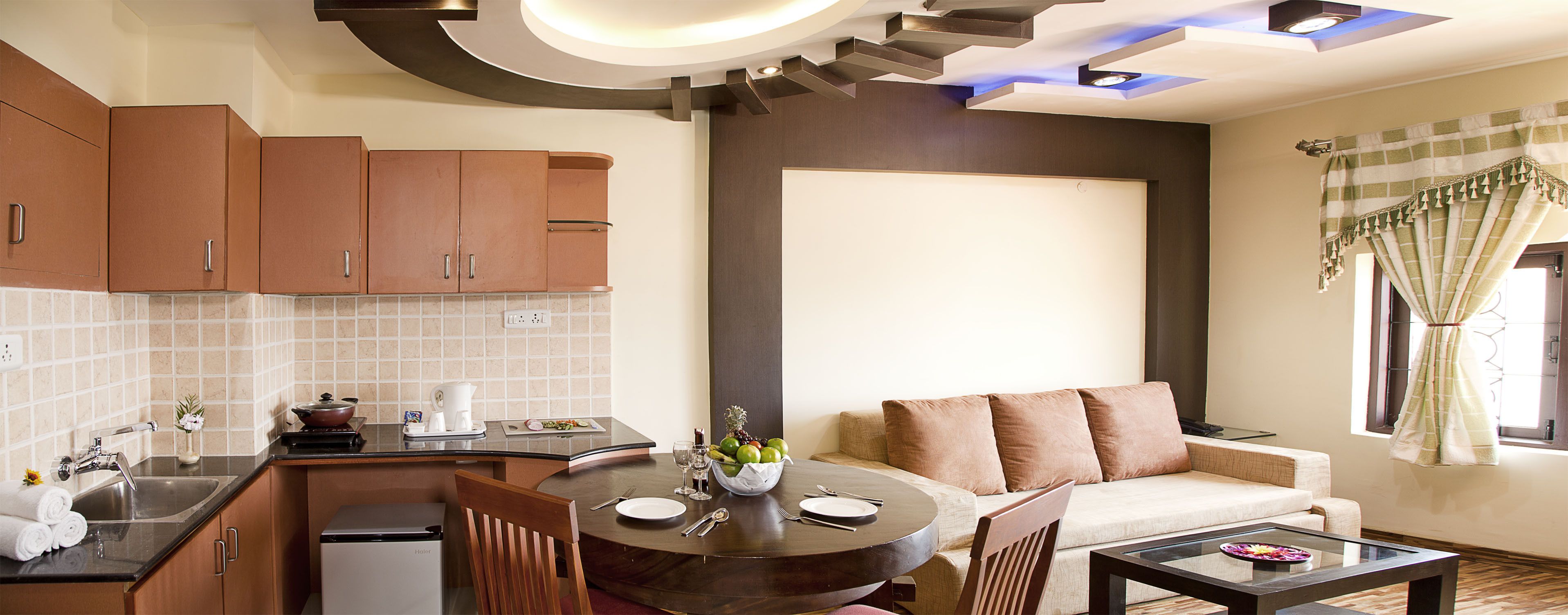 A modern kitchen with a dining area, a sofa, and a window with curtains.
