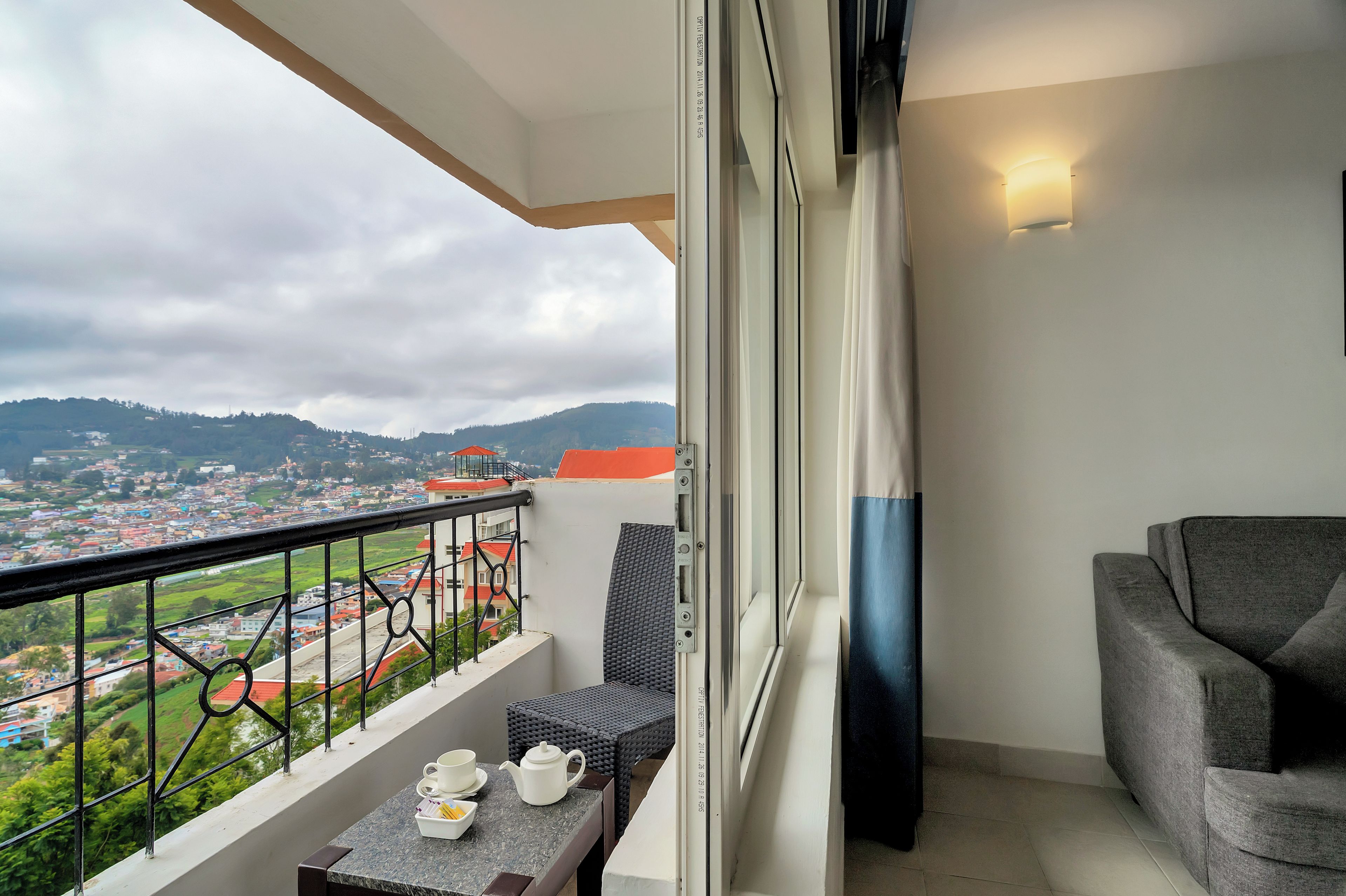 A balcony with a table, chairs, and a view of a town and hills.