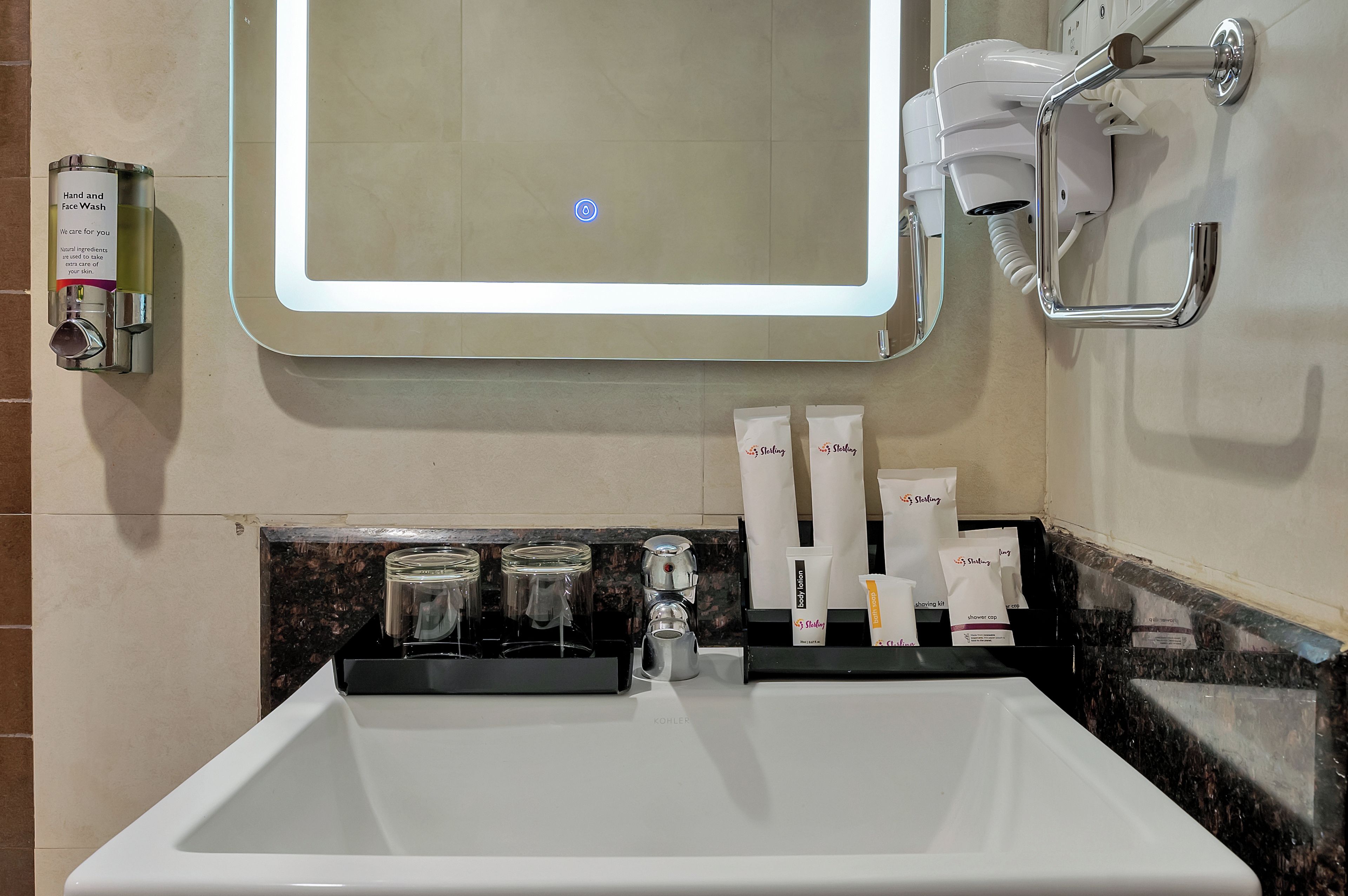 A bathroom with a sink, mirror, hand and face wash dispenser, and toiletries.