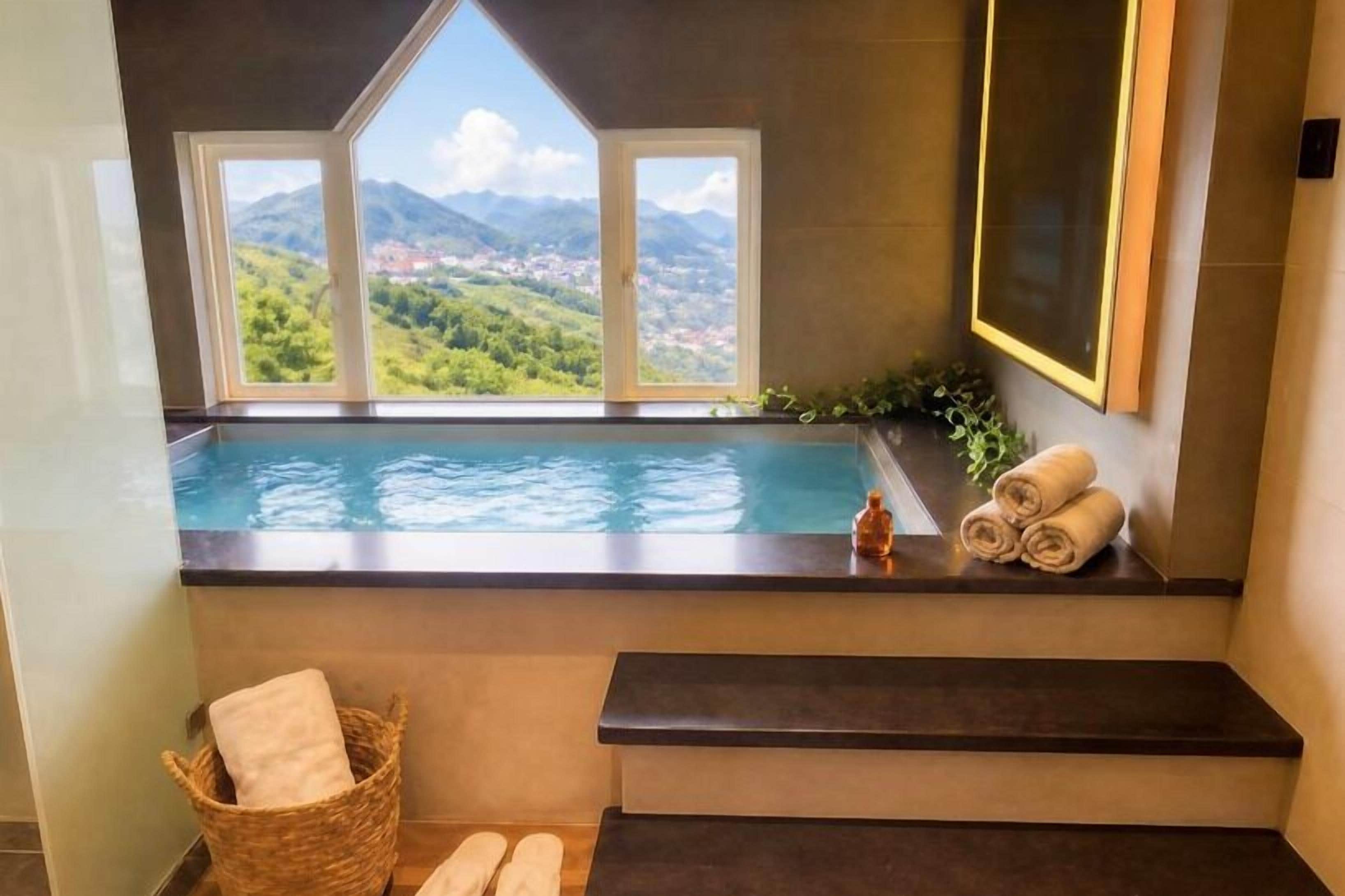 Un bagno con piscina integrata, una finestra vista montagna, uno specchio e un porta asciugamani.