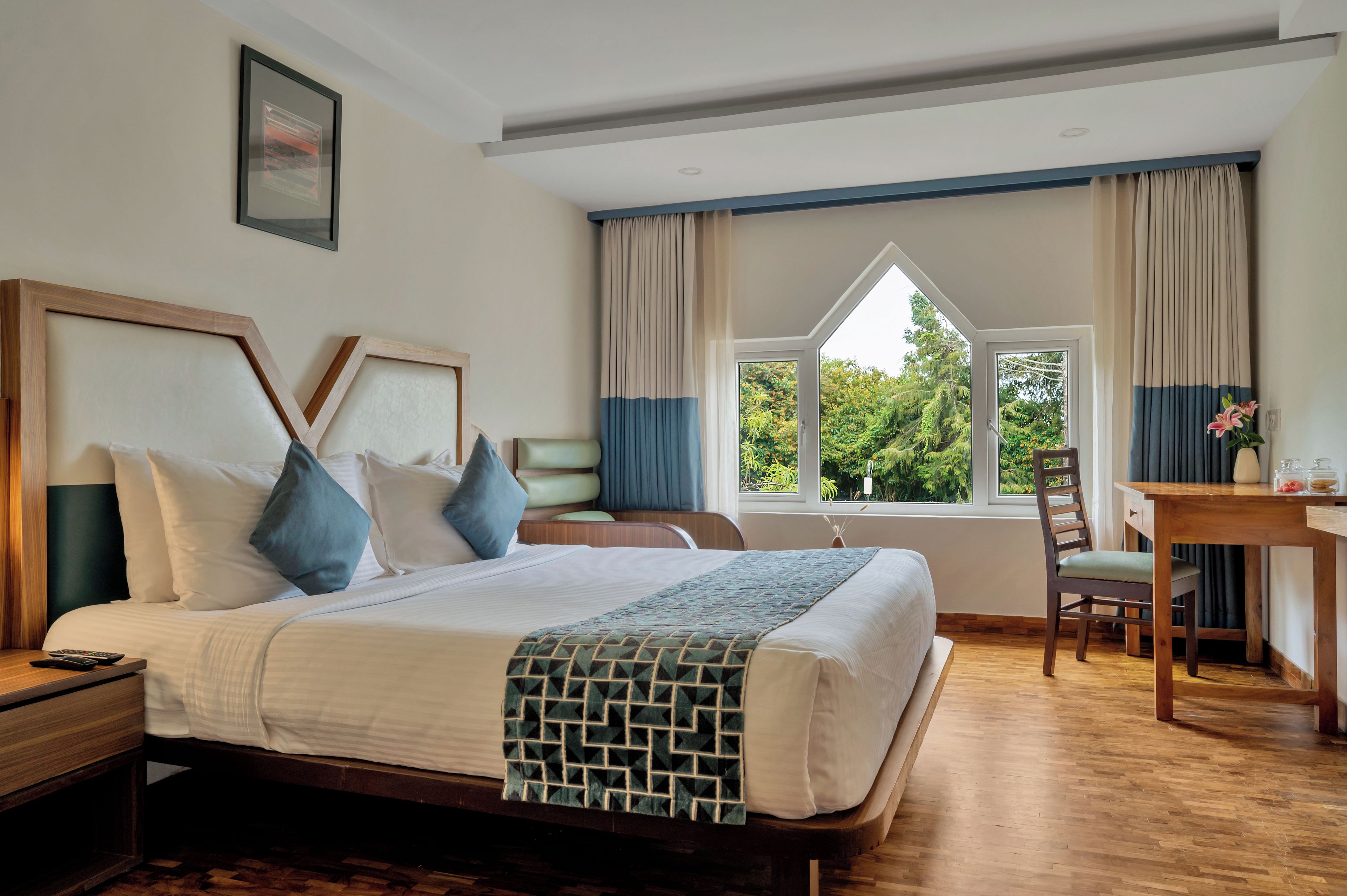 Ein Hotelzimmer mit einem großen Bett, einem Schreibtisch und Blick auf Grünfläche.