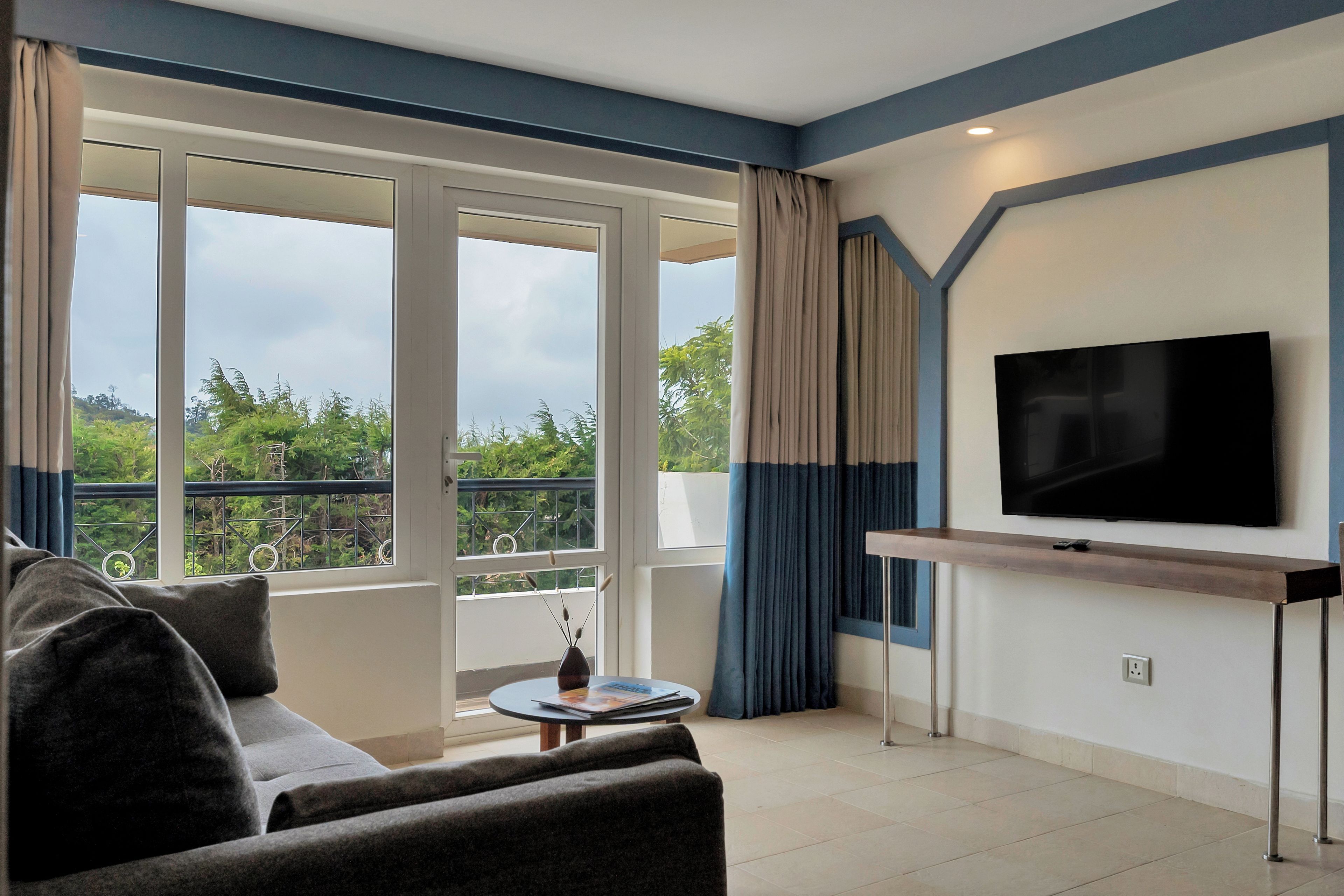 Un salon moderne avec un canapé, un téléviseur à écran plat fixé au mur et un balcon offrant une vue sur la verdure.