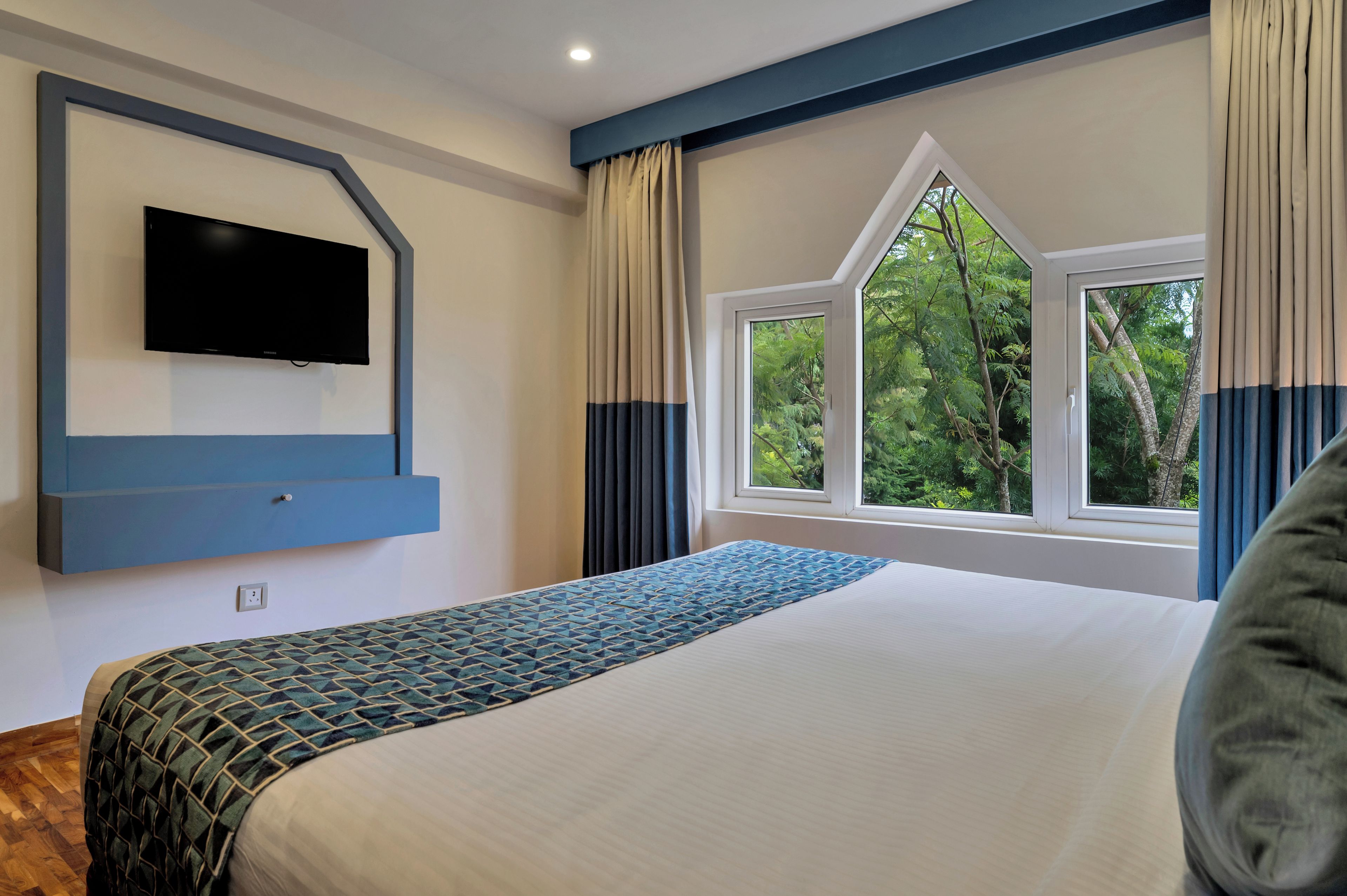 A bedroom with a bed, a television mounted on the wall, and a window with curtains.