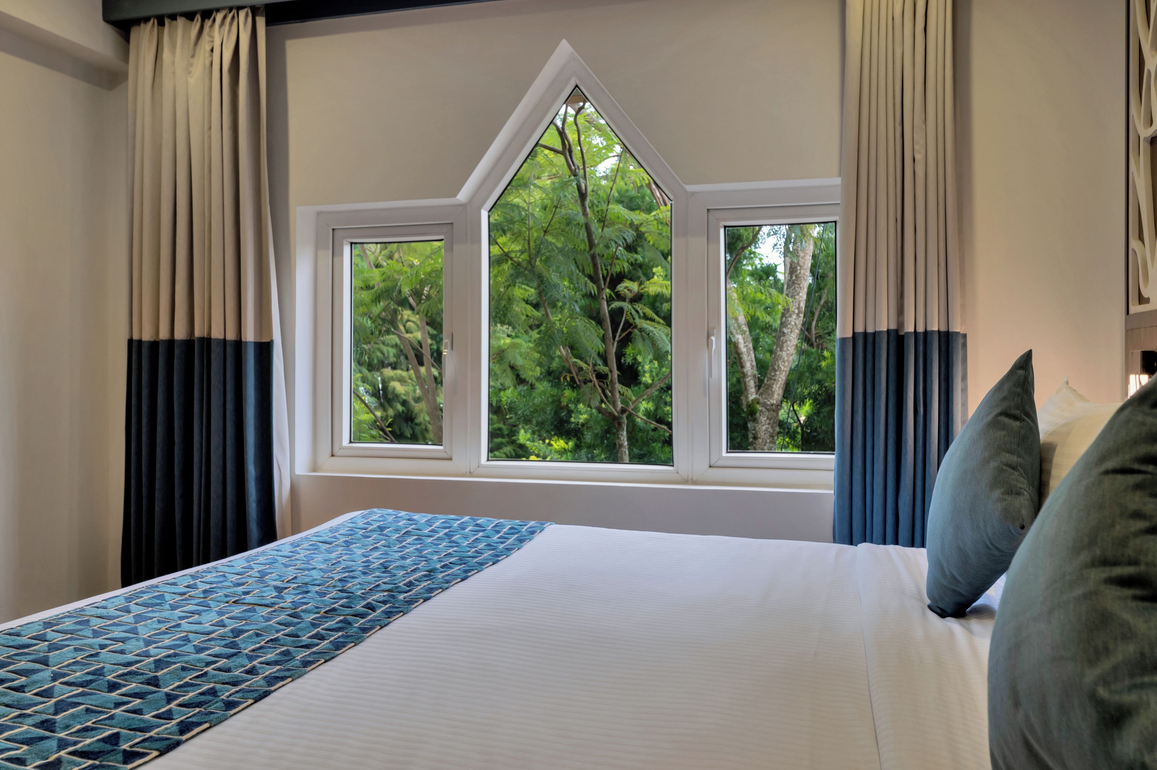 A bedroom with a large bed, two windows, and a view of trees.