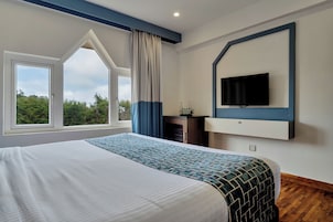 Een hotelkamer met een groot bed, een aan de muur bevestigde televisie en een raam met gordijnen.