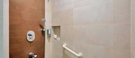 A shower area with a handheld showerhead, a wall-mounted control panel, and a grab bar.
