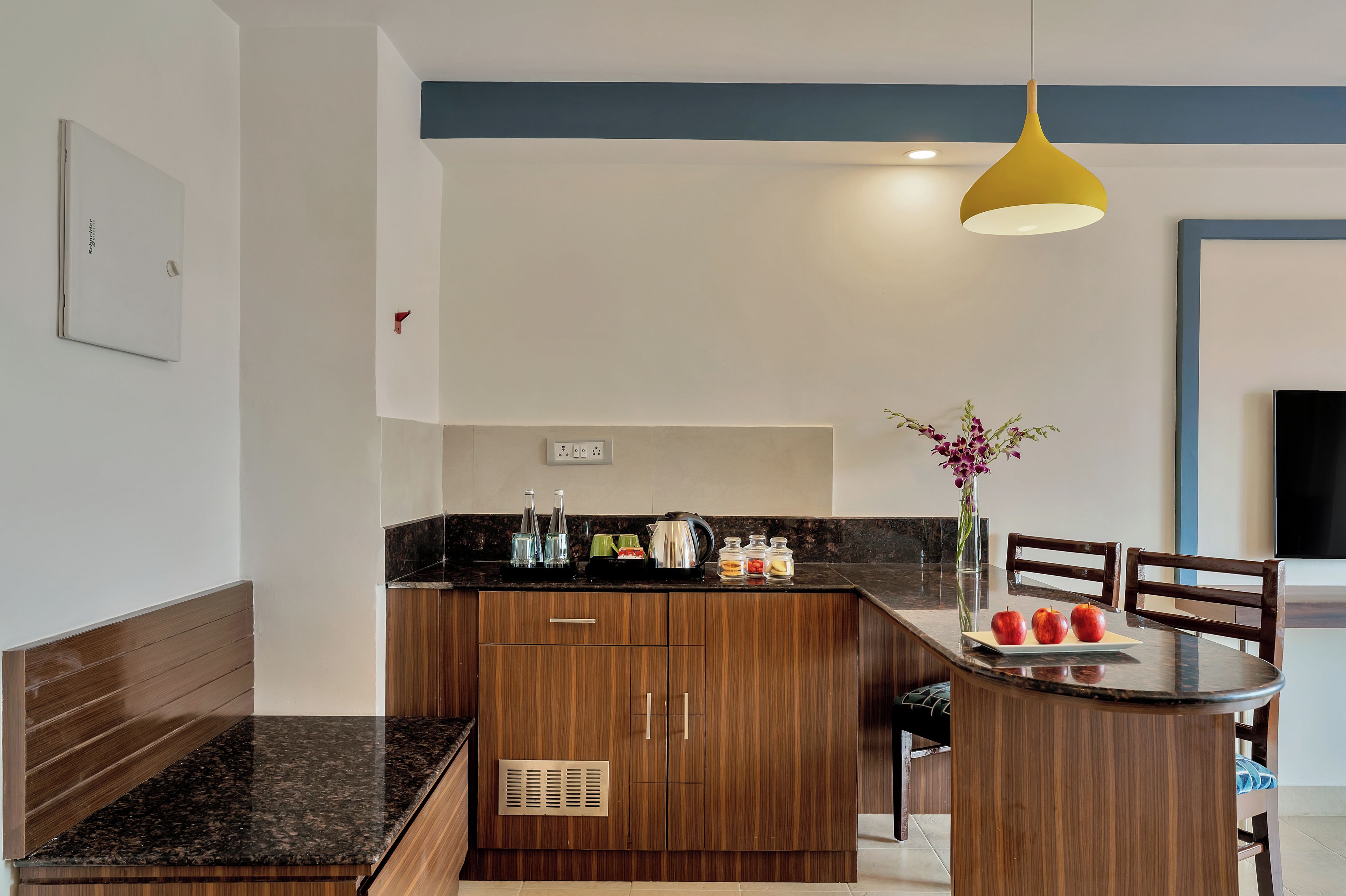 A modern kitchen with wooden cabinets, a black countertop, and a yellow pendant light.