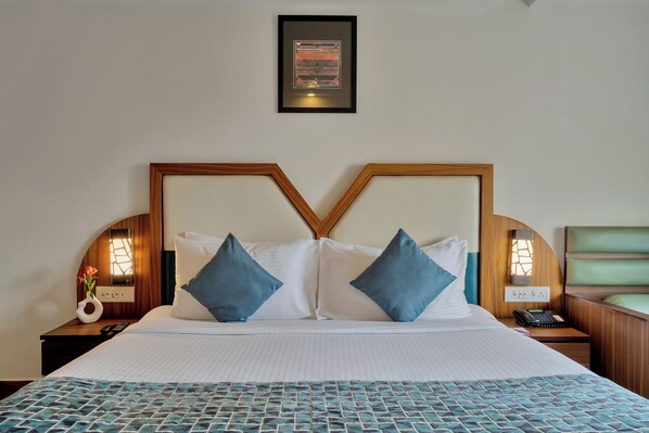 Habitación de hotel con una cama grande, dos mesitas de noche, una lámpara de noche, un jarrón con flores y un cuadro en la pared.