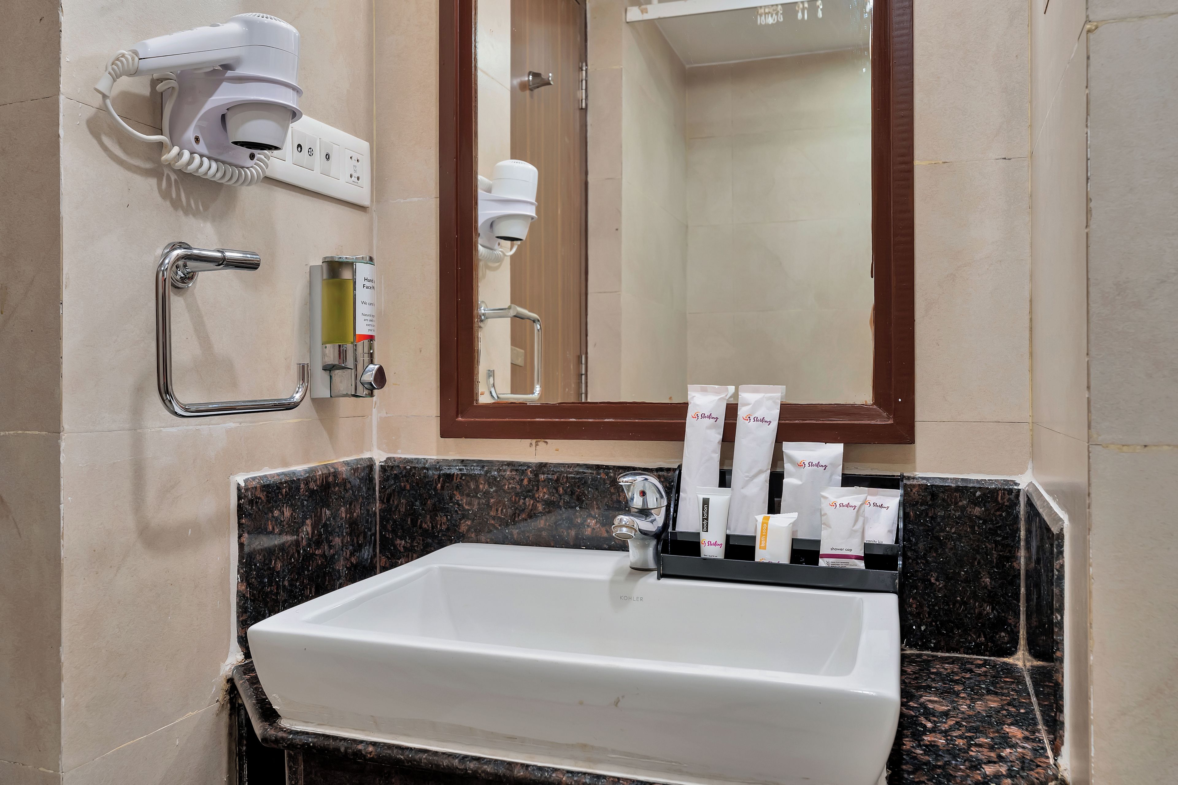 A bathroom with a white sink, a hand dryer, a hair dryer, a mirror, and toiletries.