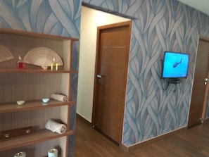 Habitación de hotel con suelo de madera, televisor montado en la pared, una puerta y un papel tapiz estampado.