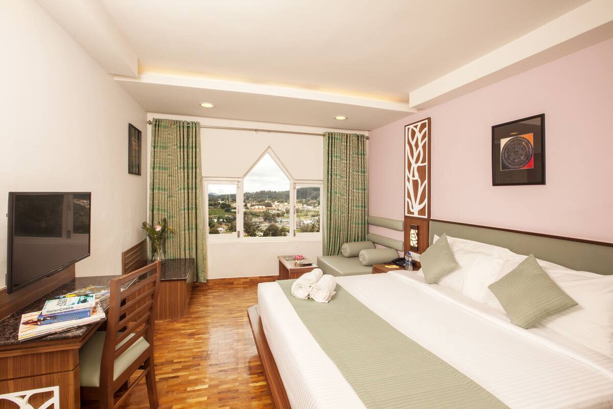 Une chambre d’hôtel avec un lit, un bureau avec une télévision, une fenêtre avec des rideaux et une vue sur l’extérieur.