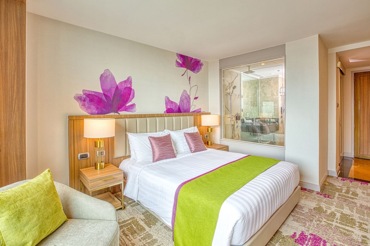 Een hotelkamer met een bed, nachtkastje, lamp, stoel en spiegel.