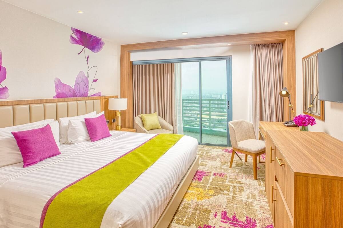 Een hotelkamer met een groot bed, een bureau, een stoel en uitzicht op de stad door het raam.