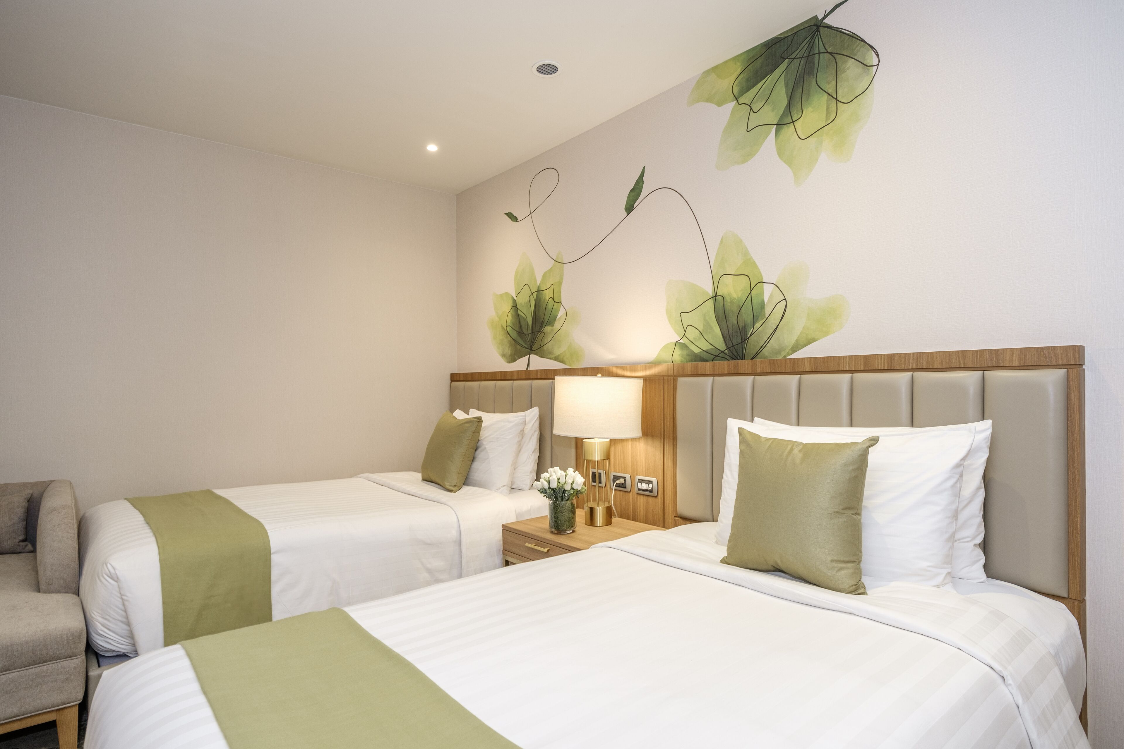 Habitación de hotel con dos camas, una mesita de noche, una lámpara y una planta colocada en la pared.