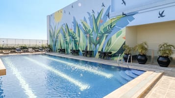 A rooftop pool with a mural of birds and plants, lounge chairs, and potted plants.