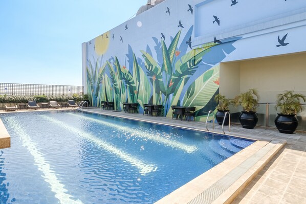 A rooftop pool with a mural of birds and plants, lounge chairs, and potted plants.