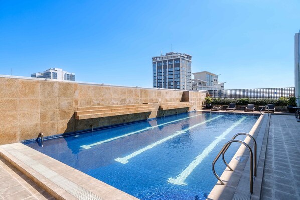 Una piscina en la azotea con agua cristalina, una escalera metálica y vistas de edificios circundantes.