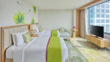 Habitación de hotel con dos camas, un televisor, una mesita con un florero y un ventanal con vistas a la ciudad.
