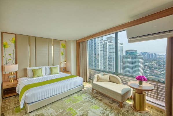 A modern hotel room with a large bed, a sofa, a round table with a vase, and a view of the cityscape.