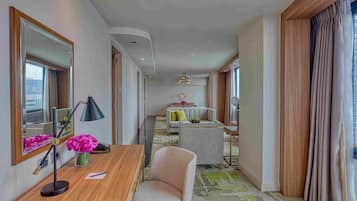 Habitación de hotel con escritorio de madera, una silla, un sofá, un espejo grande y vistas a la ciudad.